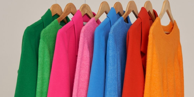 brightly coloured jumpers and jackets on hangers.