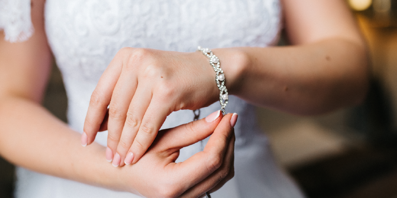 Bride putting a pearl and diamond bracelet on her wrist.
